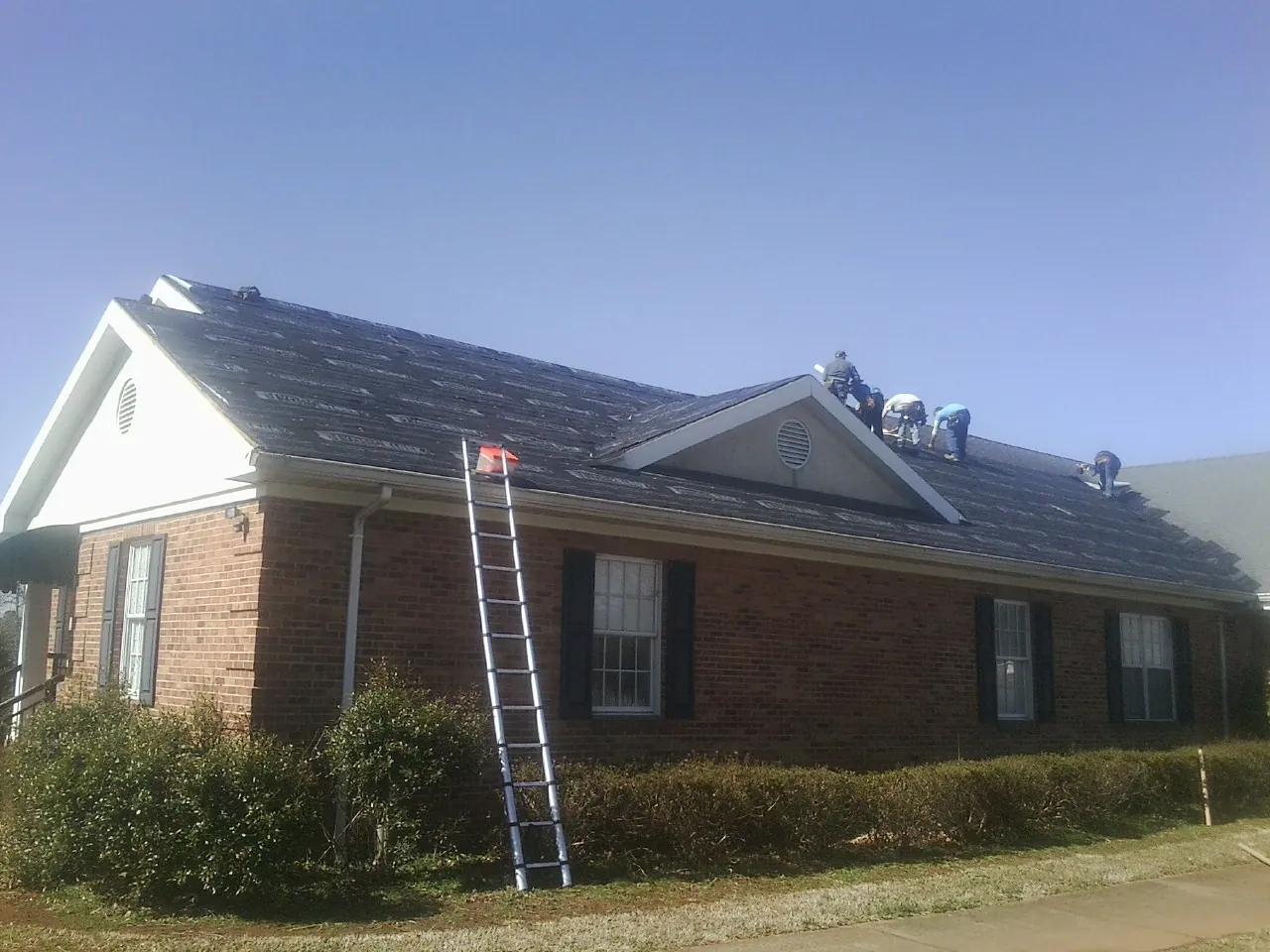 Crew tearing shingles off a brick ranch roof with a ladder set — Metal Roof Repair work by our crew in Gilberts