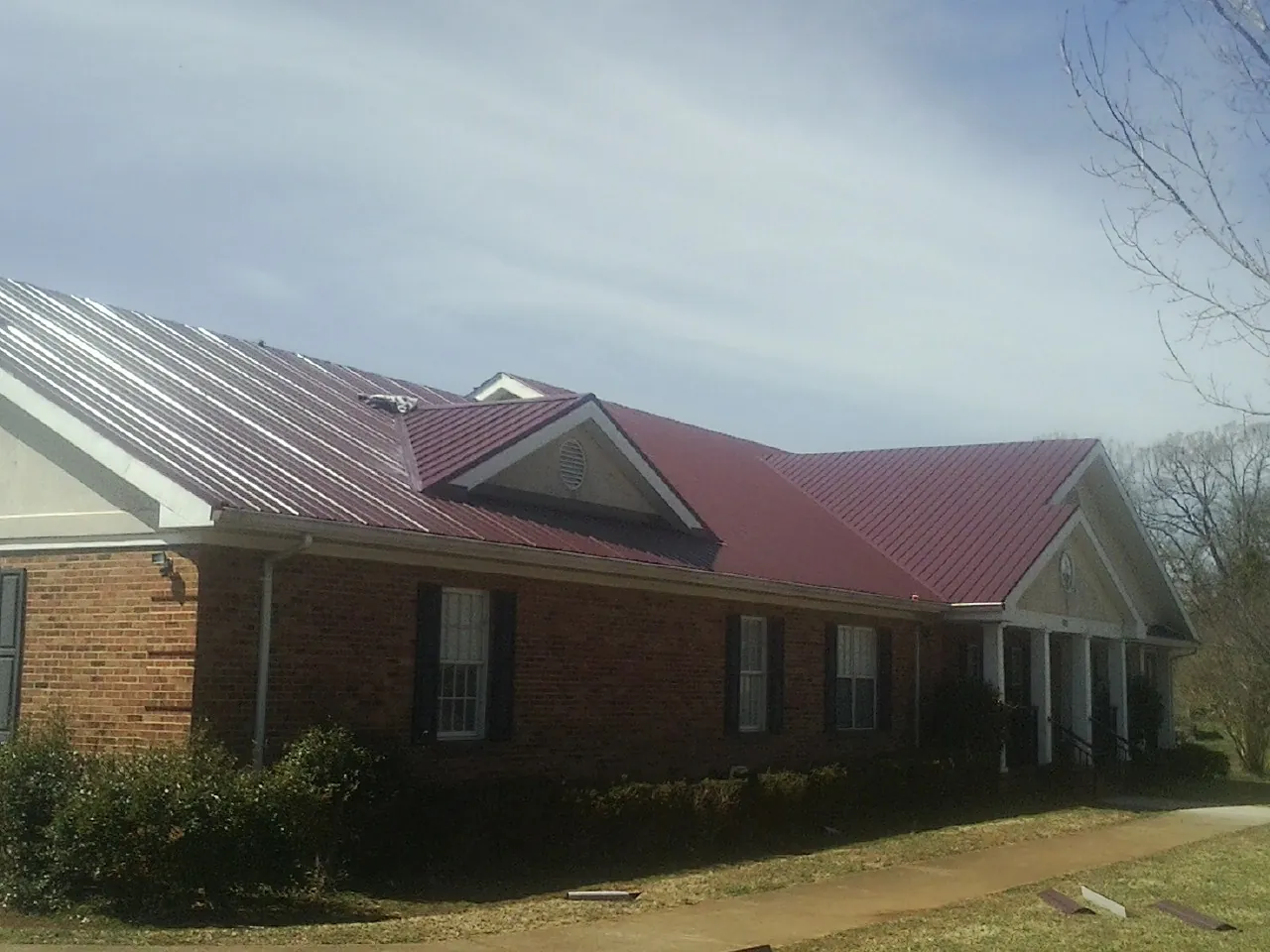 Red metal roof with gabled entries on a long brick building, from a Hail Damage Roof Repair job in Gilberts