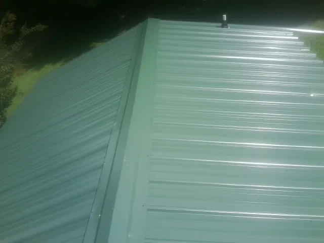 New green metal panels meeting at the ridge of a roof — Flat Roof Repair work by our crew in Gilberts