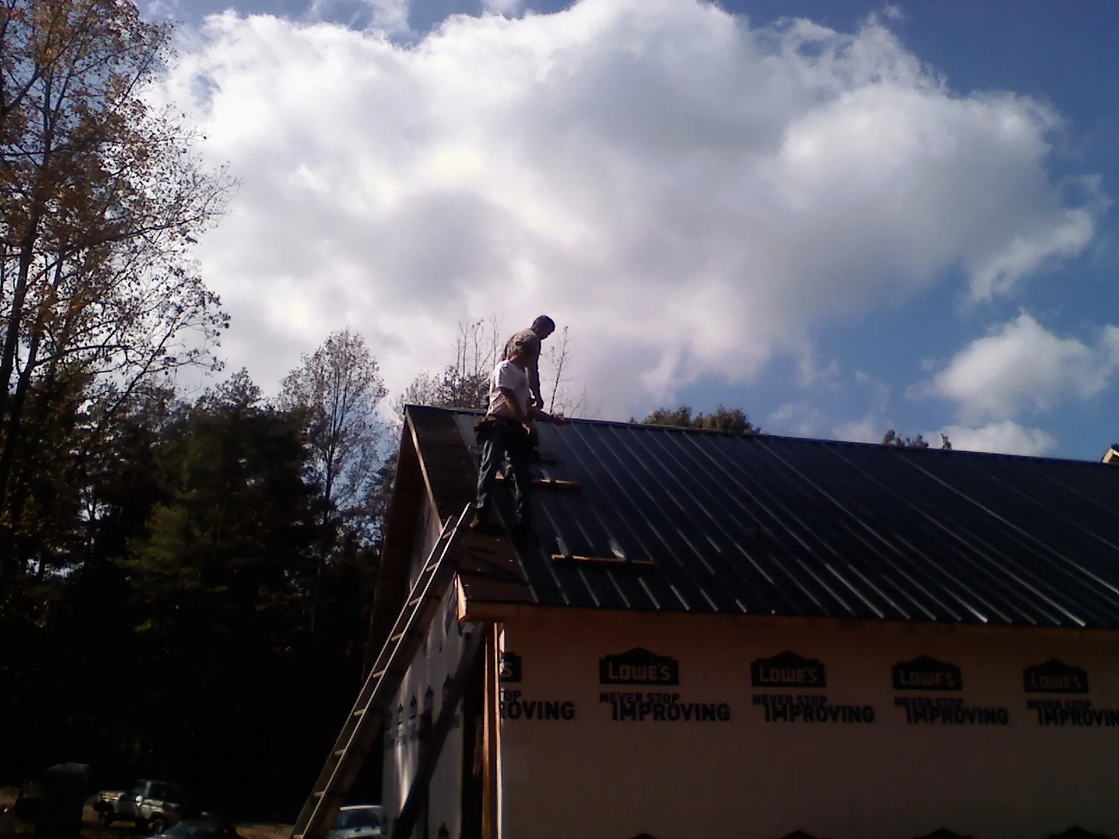 Roofer fastening dark metal panels high against a cloudy sky, from a Roof Inspection job in Gilberts